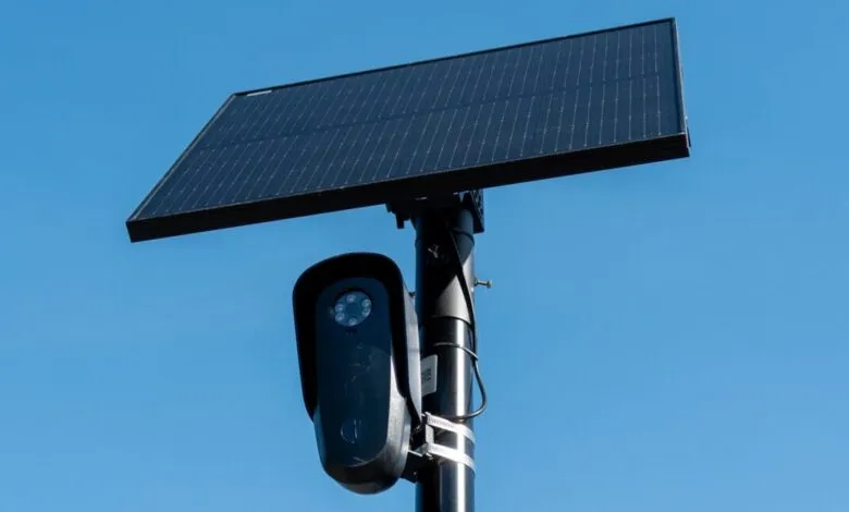 Flock license plate reader and solar panel mounted on a pole against a clear blue sky.