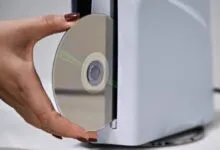 Close-up of a hand inserting a compact disc into a white electronic console slot.