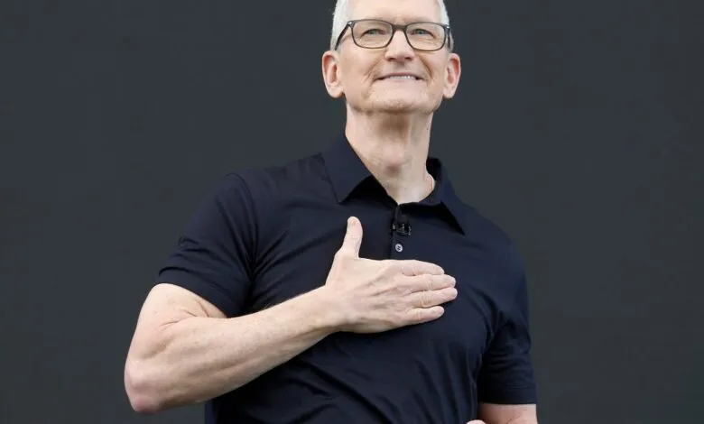 Apple CEO Tim Cook smiling warmly with his hand placed on his chest against a dark backdrop