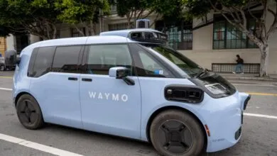 A light blue Waymo autonomous ride-hailing vehicle parked on a city street.