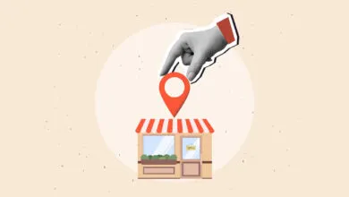 A grayscale hand places a red location pin onto a small illustrated storefront.