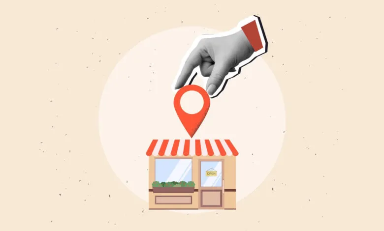 A grayscale hand places a red location pin onto a small illustrated storefront.