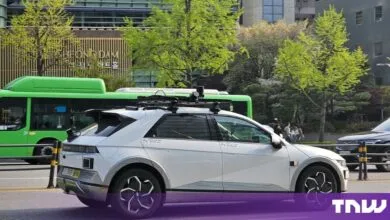 White Hyundai Ioniq 5 Robotaxi navigating a city street in Seoul with roof-mounted sensors.