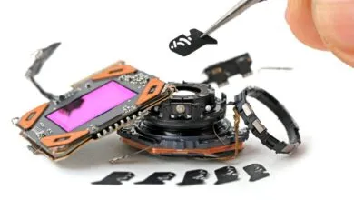 Tweezers carefully lift a small component from disassembled smartphone camera parts.