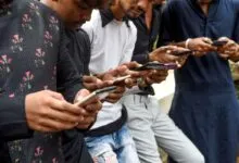 Young Indian men stand together outdoors, deeply engaged with their smartphones.