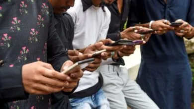 Young Indian men stand together outdoors, deeply engaged with their smartphones.