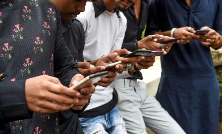 Young Indian men stand together outdoors, deeply engaged with their smartphones.