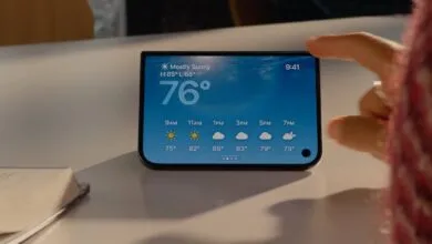 A hand interacts with a smartphone displaying a detailed weather app interface on a white table.