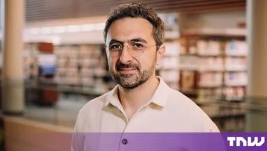 Portrait of Mustafa Suleyman wearing round glasses and a light-colored button-down shirt.