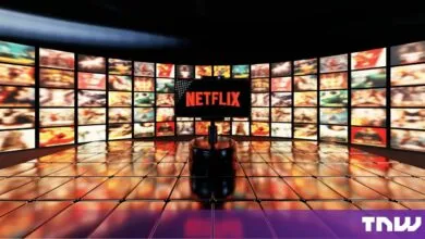 Netflix logo displayed on a smartphone amidst a large curved wall of multiple glowing screens.
