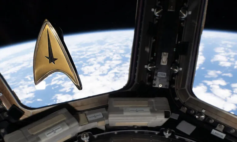 A gold Star Trek command insignia pin floats inside a spacecraft window overlooking Earth's horizon.