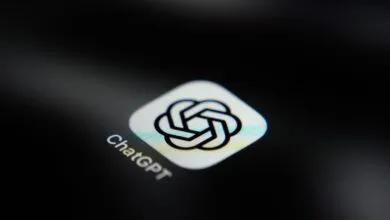 Close-up of the ChatGPT app icon glowing brightly on a dark smartphone screen in low light.