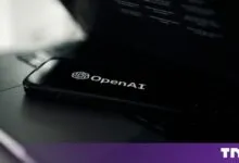 Smartphone displaying the OpenAI logo resting on a black laptop keyboard