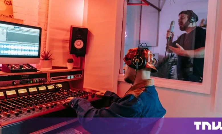 Sound engineer at a mixing desk while a vocalist sings in a studio booth