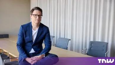 Ruben Bryon sitting on a conference table wearing a blue blazer and glasses.