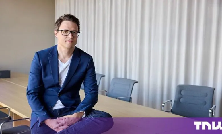 Ruben Bryon sitting on a conference table wearing a blue blazer and glasses.