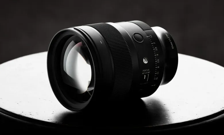 Close-up of a sleek black camera lens resting on a dark circular surface against a moody background.