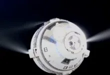 Boeing Starliner spacecraft in orbit with thrusters firing against a black space background.