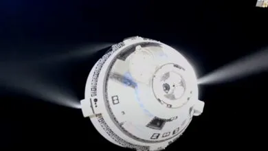 Boeing Starliner spacecraft in orbit with thrusters firing against a black space background.