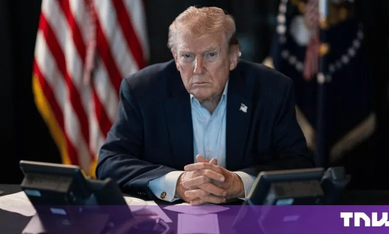 President Donald Trump sits at a desk with American flags in the background, looking directly forward.