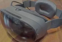 Close-up of a black VR headset resting on a wooden floor, highlighting its curved visor and strap.