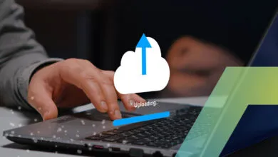 Close-up of hands on a laptop keyboard with a white cloud and blue upload icon floating above.