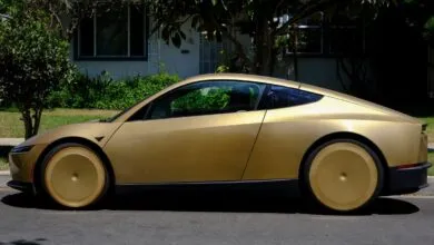 Profile view of a sleek, metallic gold Tesla Cybercab parked on a residential street.