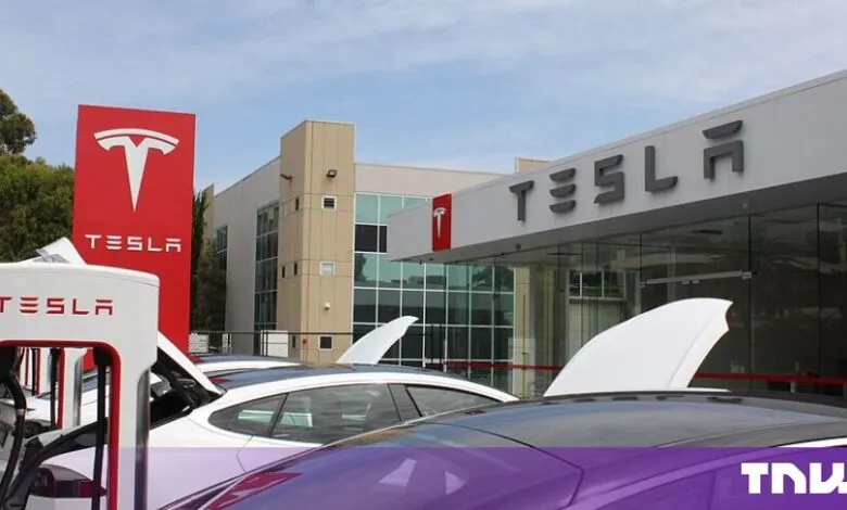 Exterior view of a Tesla dealership and charging station with parked electric cars.