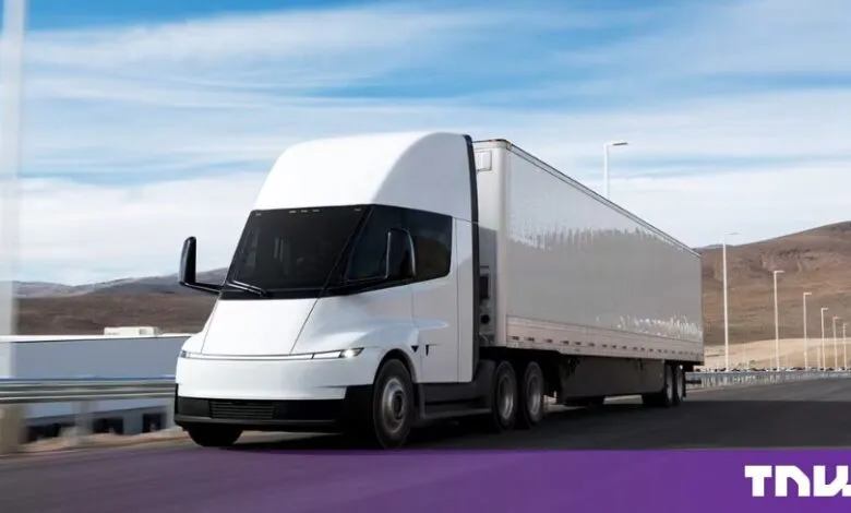 A sleek, white Tesla Semi electric truck drives along a highway against a blue sky.