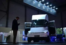 A white Tesla Semi electric truck parked on a showroom floor beneath a glowing Tesla sign.