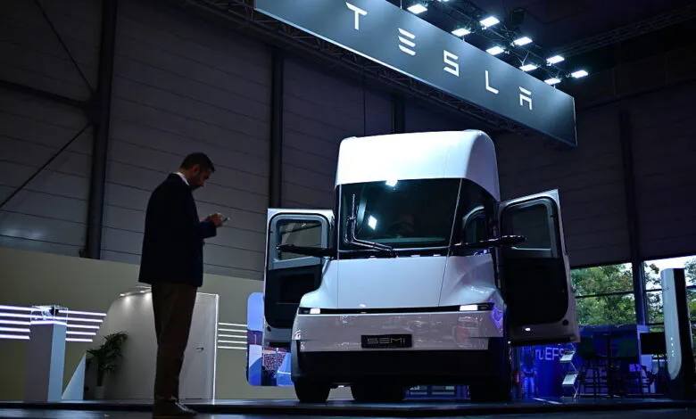 A white Tesla Semi electric truck parked on a showroom floor beneath a glowing Tesla sign.