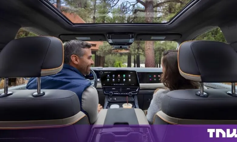 Man and woman sitting in the front seats of a luxury vehicle featuring a large central touchscreen.