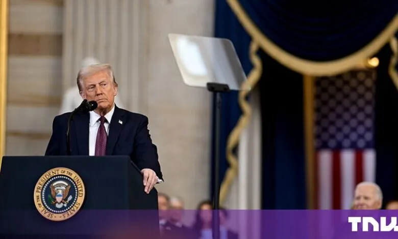 Donald Trump standing at a presidential podium with a US flag in the background.