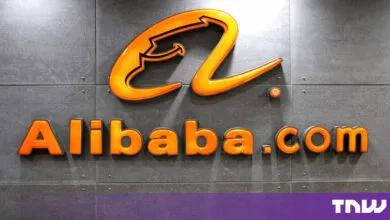 Bright orange Alibaba.com logo mounted on a dark textured grey wall