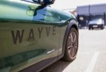 Close-up of a green autonomous vehicle branded with the Wayve logo parked outside.