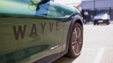 Close-up of a green autonomous vehicle branded with the Wayve logo parked outside.
