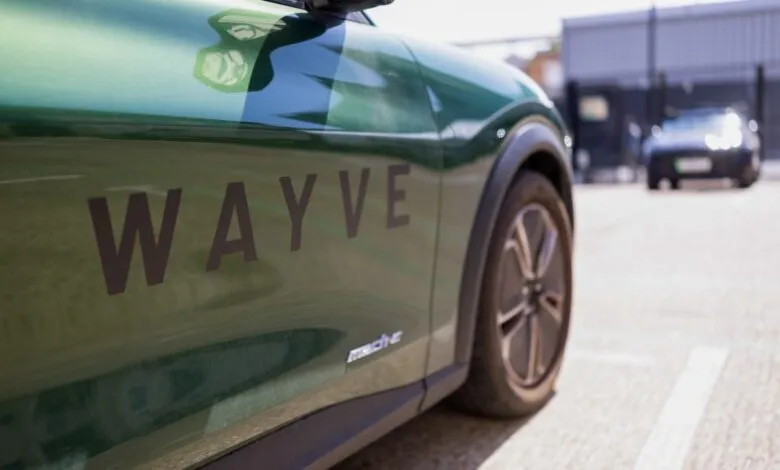 Close-up of a green autonomous vehicle branded with the Wayve logo parked outside.