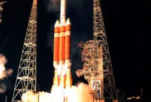 A large rocket launches at night, surrounded by towering gantry structures and brilliant exhaust flames.