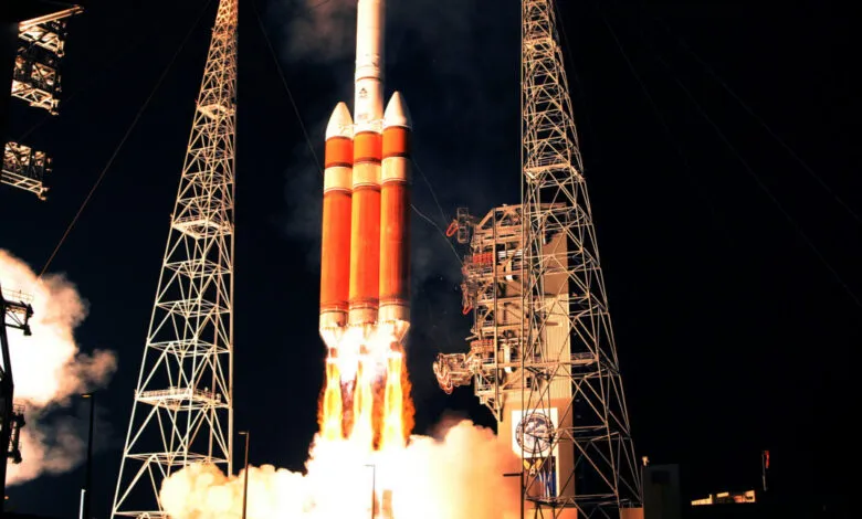 A large rocket launches at night, surrounded by towering gantry structures and brilliant exhaust flames.