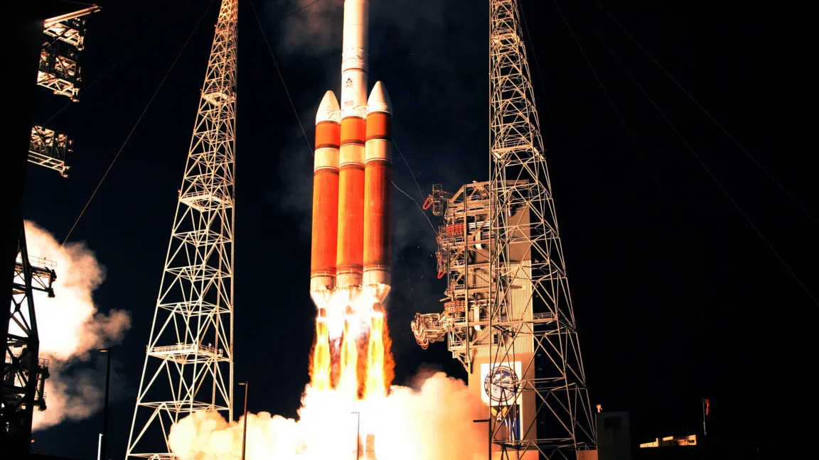 A large rocket launches at night, surrounded by towering gantry structures and brilliant exhaust flames.