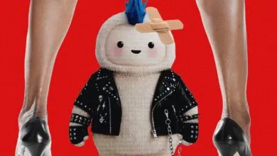 A cute, fuzzy plush toy with a blue mohawk, studded leather jacket, and adhesive bandages on its head.