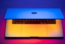 A MacBook Pro laptop with keyboard and trackpad illuminated by vibrant blue and orange studio lighting.