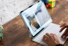 A person types on a white Magic Keyboard attached to an Apple iPad Pro on a wooden desk.