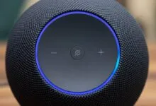Close-up of a black smart speaker with a glowing blue light ring and control buttons.
