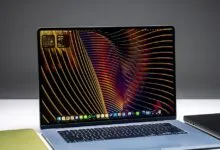 An Apple laptop open on a white desk displays a vibrant abstract screen wallpaper.