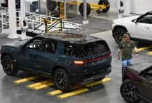 Rivian CEO RJ Scaringe walking past electric SUVs on the factory assembly floor.