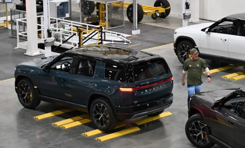 Rivian CEO RJ Scaringe walking past electric SUVs on the factory assembly floor.