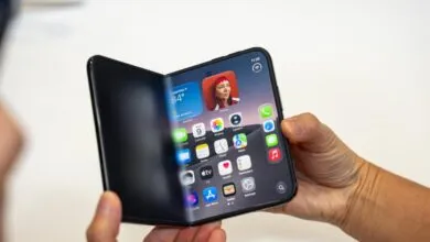 Hands holding a futuristic foldable smartphone with a flexible OLED display showing iOS apps.