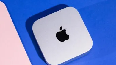 Silver Apple Mac Mini desktop computer resting on a vibrant blue surface next to a pink accent.