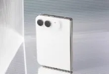A sleek white foldable smartphone with dual horizontal cameras stands inside a textured glass display box.